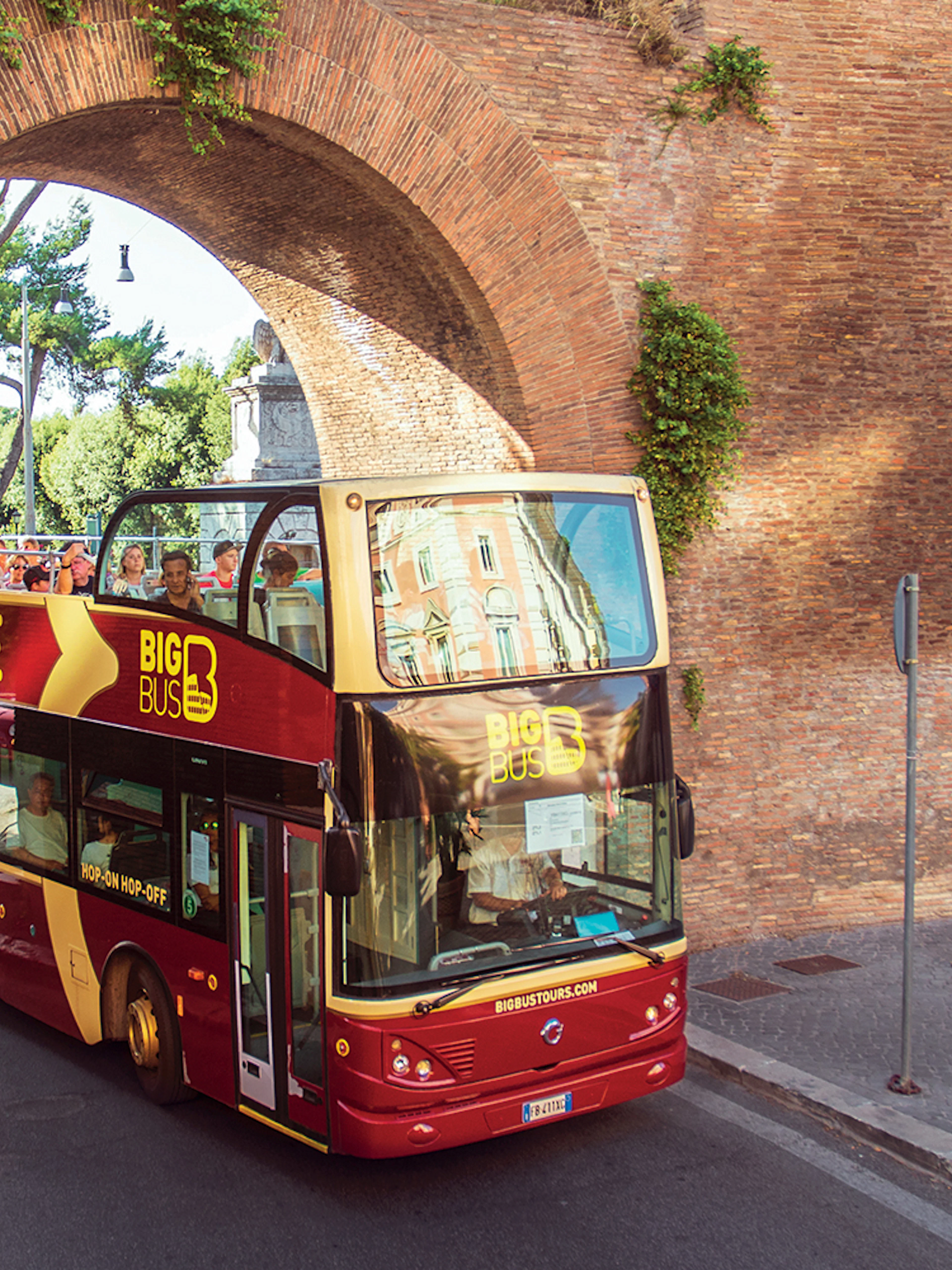 Open-top bus passing through ancient Roman archway on Big Bus Tours Rome.