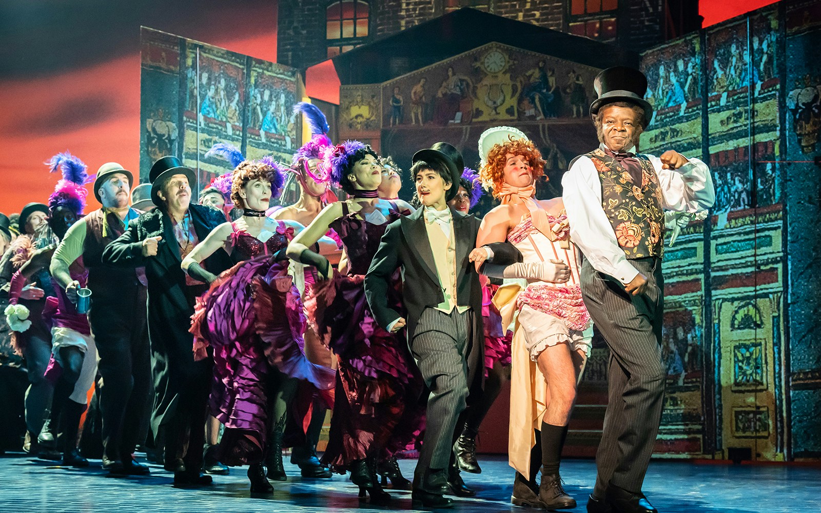 Performers in vibrant costumes dancing on stage in a scene from My Fair Lady.