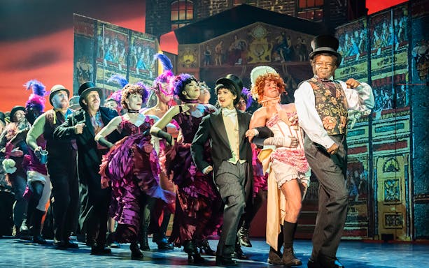 Performers in vibrant costumes dancing on stage in a scene from My Fair Lady.