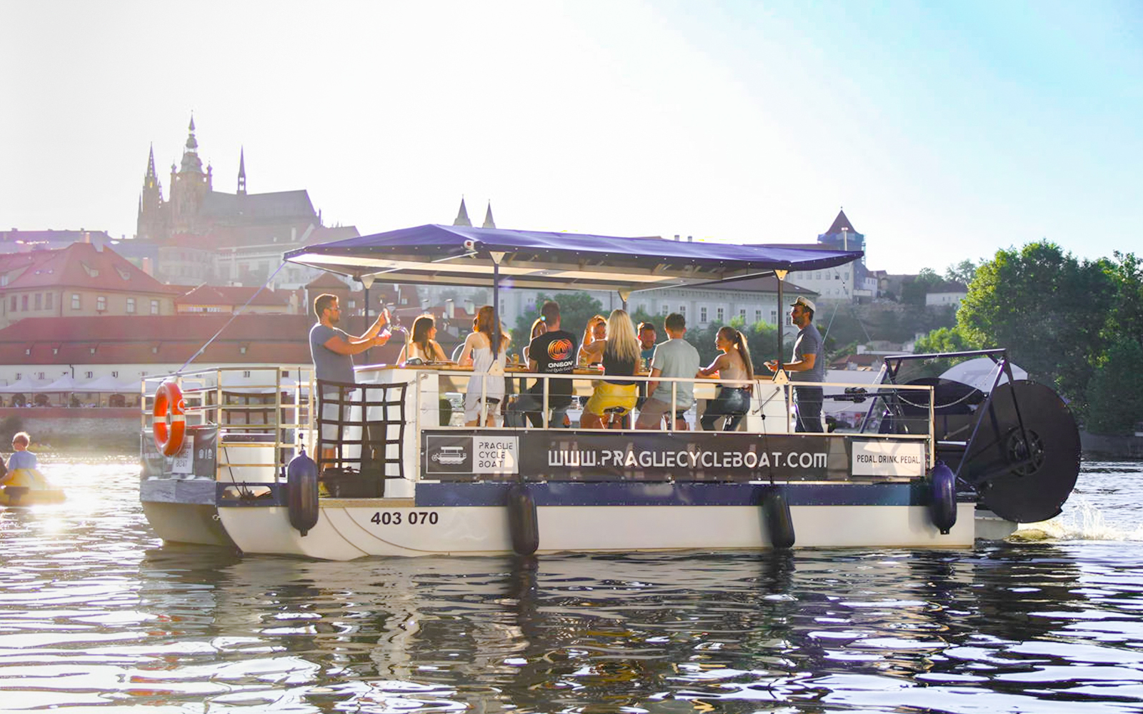 Group enjoying a Prague cycle boat tour with Prague Castle in the background.