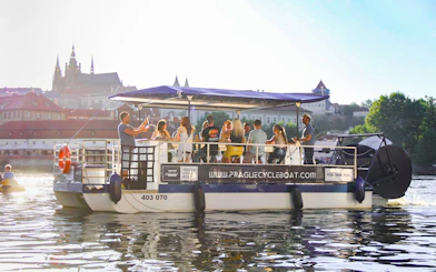 Group enjoying a Prague cycle boat tour with Prague Castle in the background.