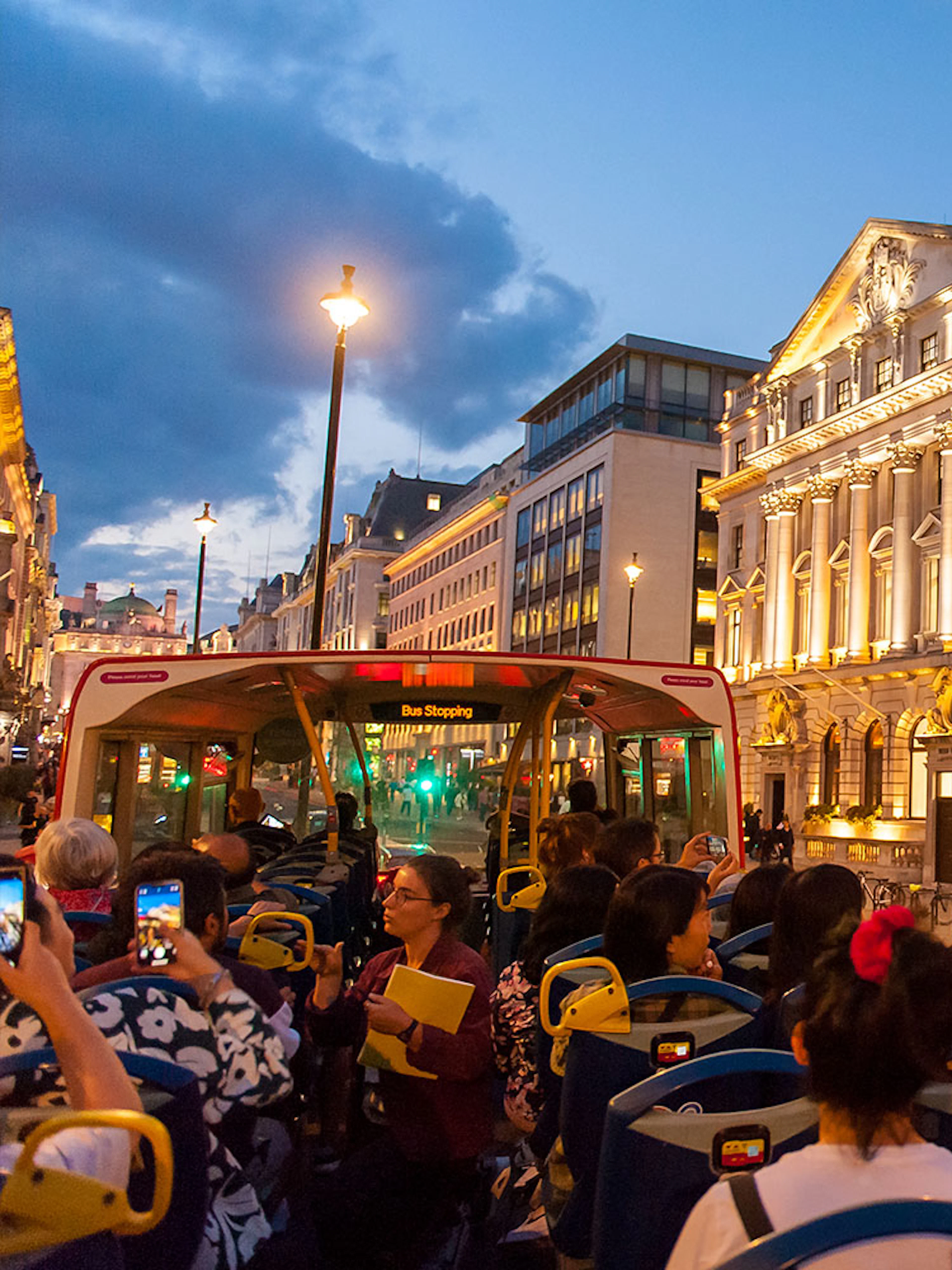 Open-top bus tour in London passing illuminated historic buildings at dusk.
