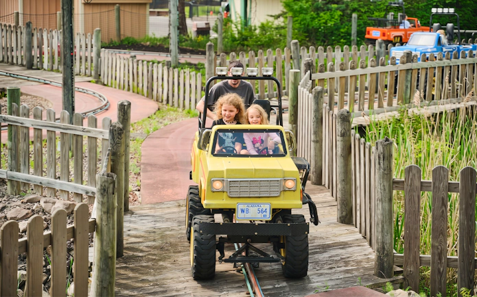 Children driving a yellow jeep on the Tree Stump Turnpike ride at Six Flags Darien Lake.