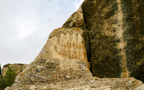 Petroglyphs on rock surface at Gobustan, Baku, depicting ancient human figures.