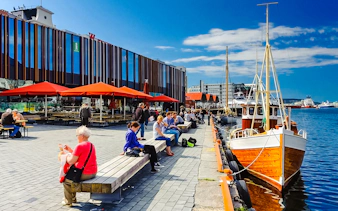 Bergen Fish Market waterfront with people sitting and boats docked nearby.