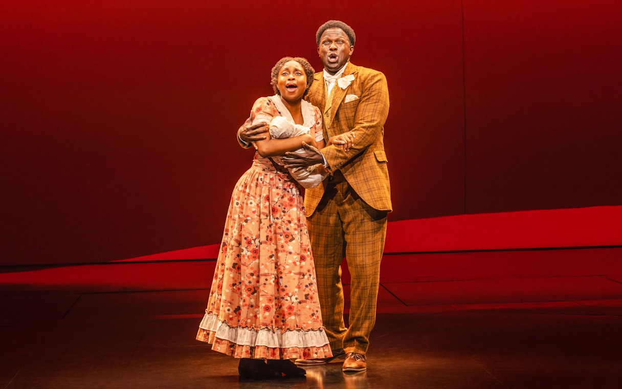 Performers singing in a scene from the musical Ragtime, holding a baby on stage.