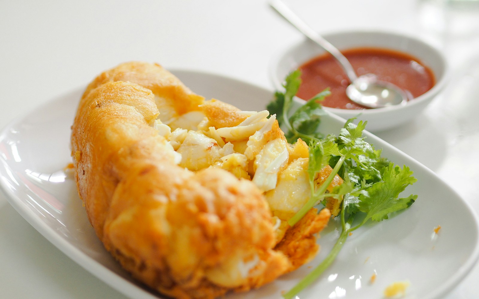 Thai style crab omelet on white plate with cilantro and dipping sauce.