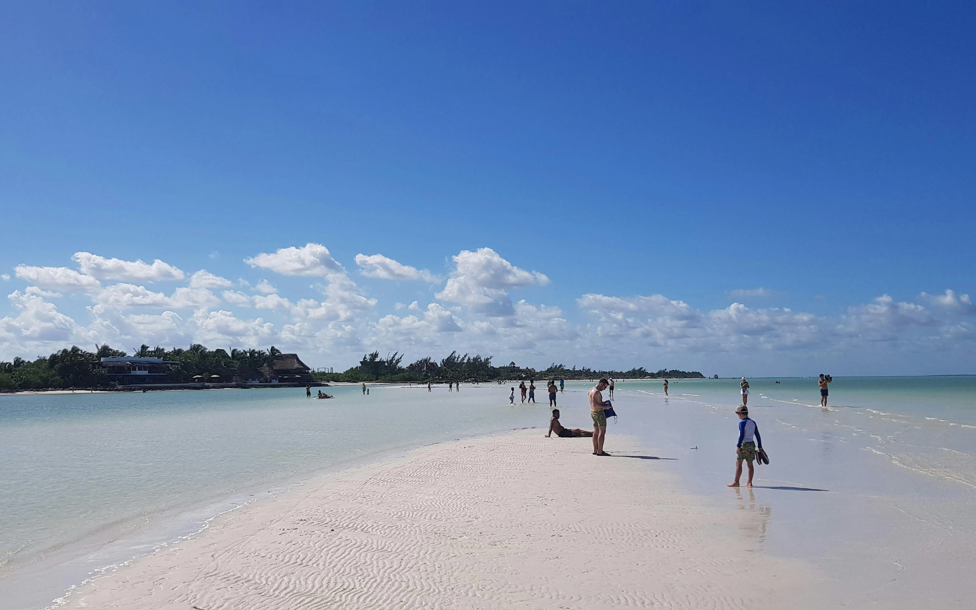 People enjoying the beach on Isla Holbox, Mexico, with clear skies and calm waters.