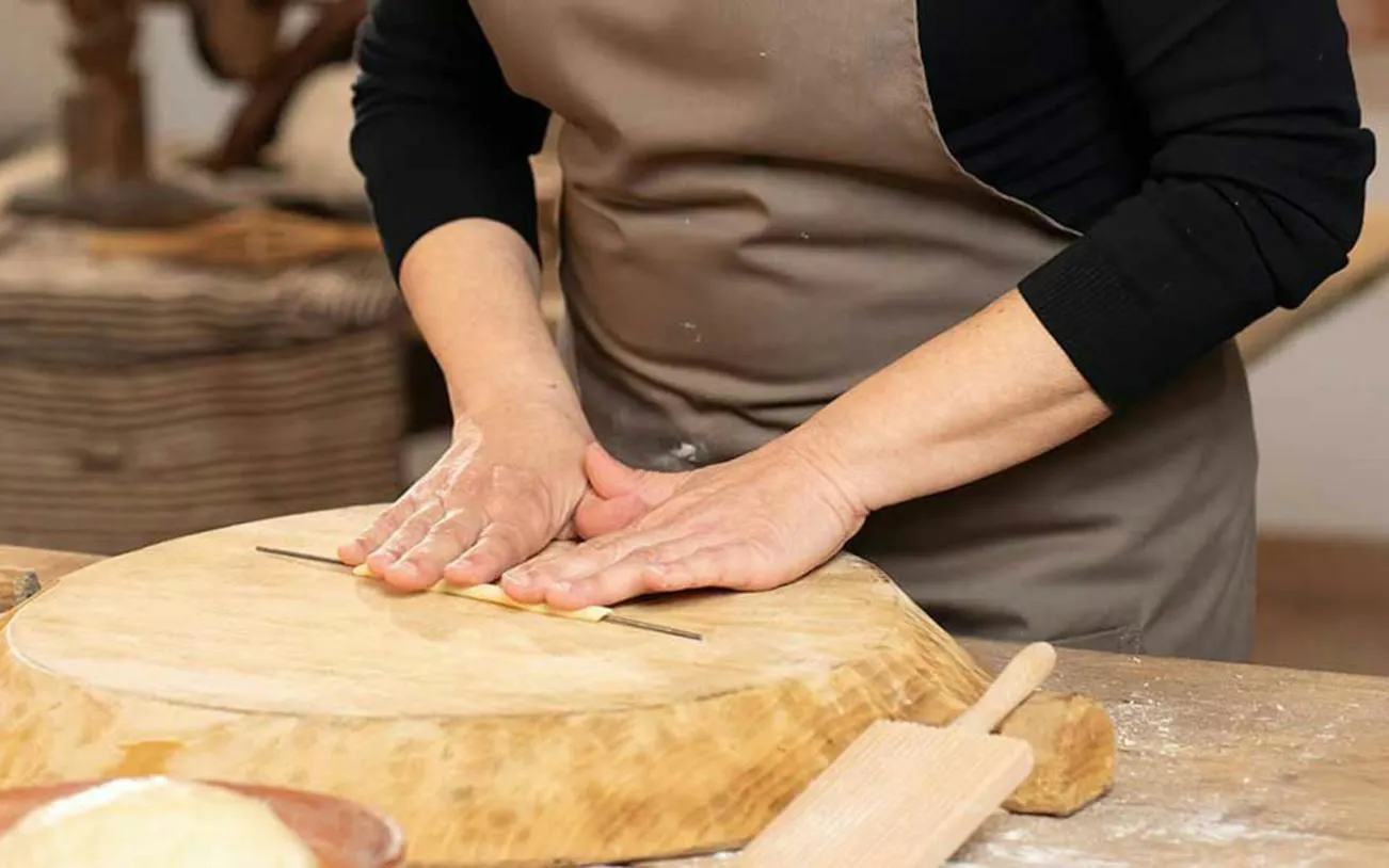 Hands shaping pasta dough on a wooden board during a workshop in Orosei, Nuoro.