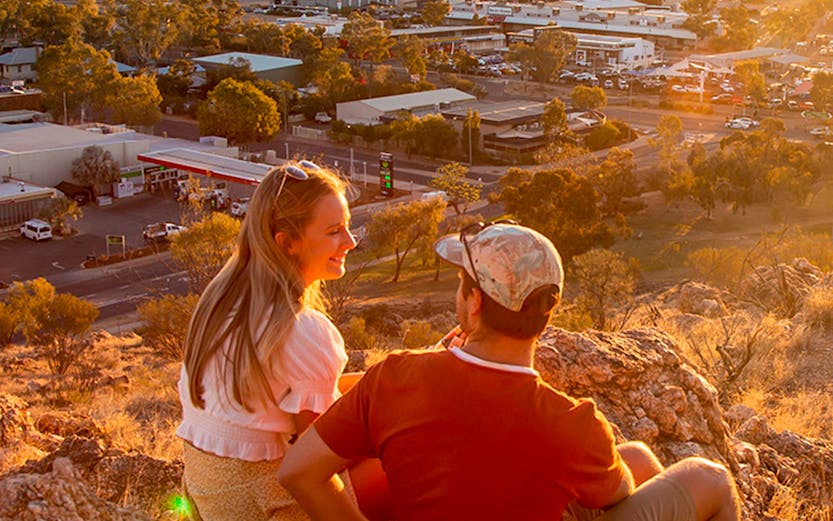 Couple enjoying sunset view over Alice Springs from a rocky hilltop.