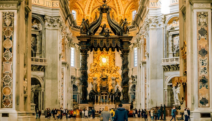 Visitors exploring the interior of St. Peter's Basilica, Vatican City, with ornate architecture and religious art.