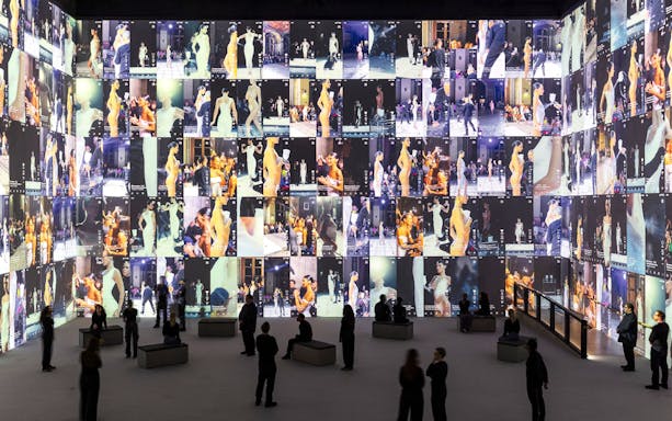 Fashion exhibit with large screens displaying runway models at Vogue: Inventing the Runway event.