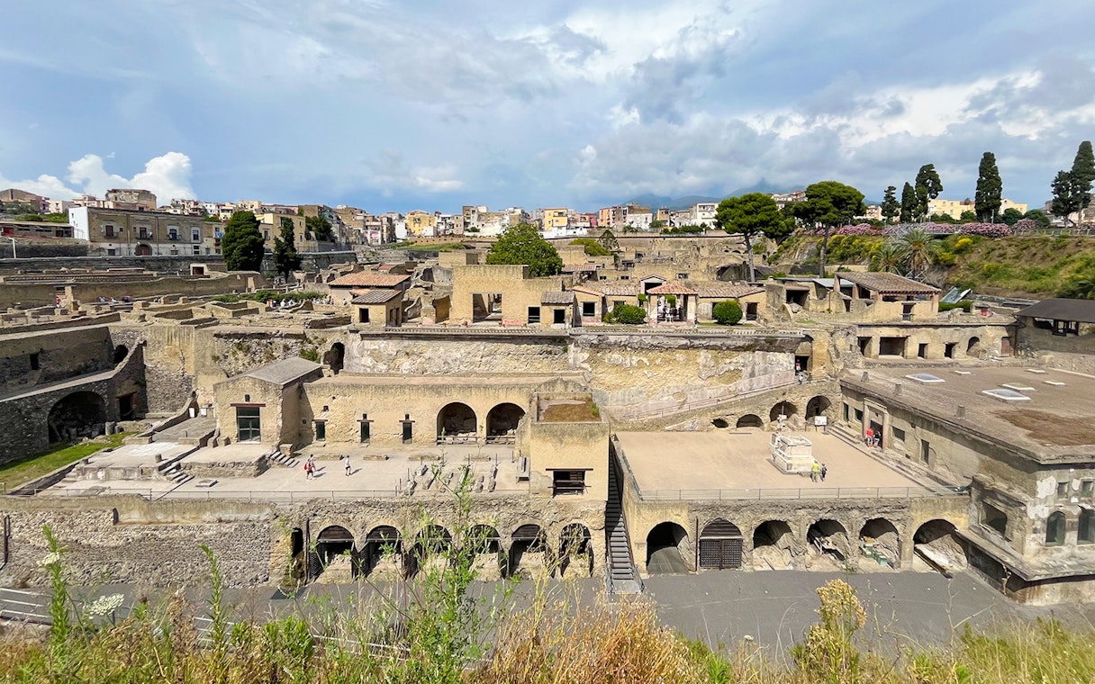 Aerial view of ancient ruins in Herculaneum, Italy, with surrounding buildings and greenery.