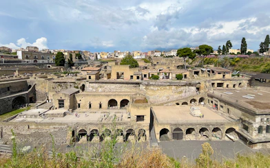 Aerial view of ancient ruins in Herculaneum, Italy, with surrounding buildings and greenery.