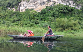 Boat ride on a river in Tam Coc, Ninh Binh, with limestone cliffs and lush greenery in the background.