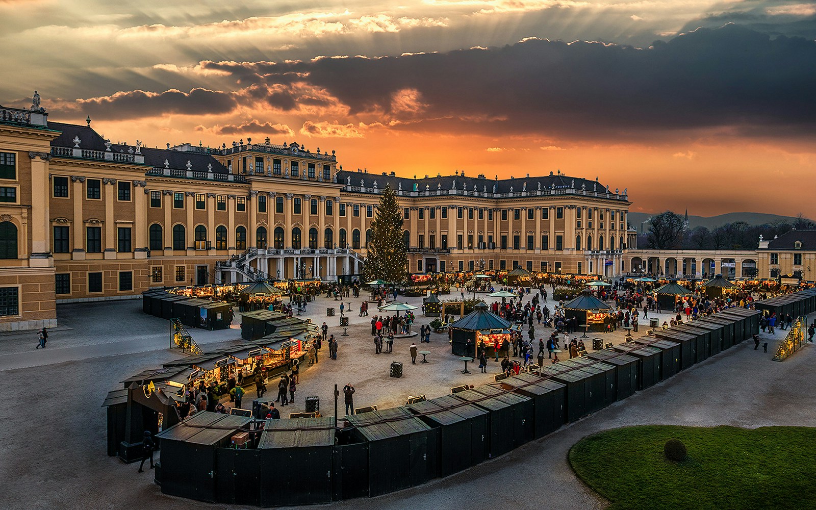 Schonbrunn Palace exterior with festive market and visitors at sunset.