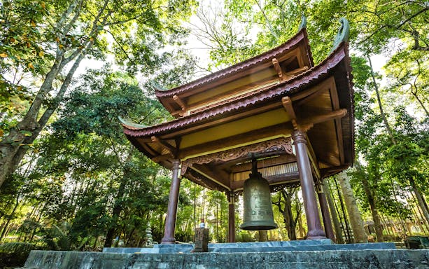 Tu Hieu Pagoda bell pavilion surrounded by lush trees in Hue, Vietnam.