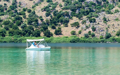 Person on pedal boat at Lake Kournas with forested hills in Crete.
