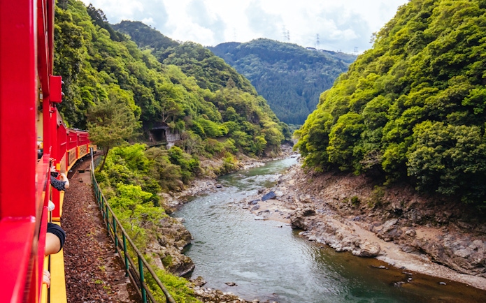 Sagano Scenic Railway train traveling along the Hozugawa River in lush green valley.