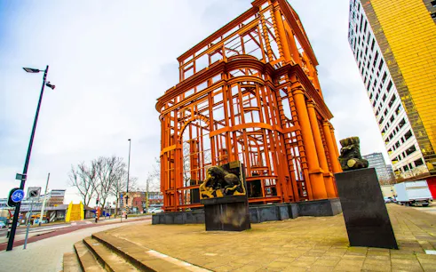 Orange steel structure with lion statues in Rotterdam, part of the Spy Hunt city exploration game.
