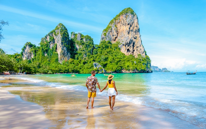 Couple walking on Railay Beach with limestone cliffs in Krabi, Thailand.