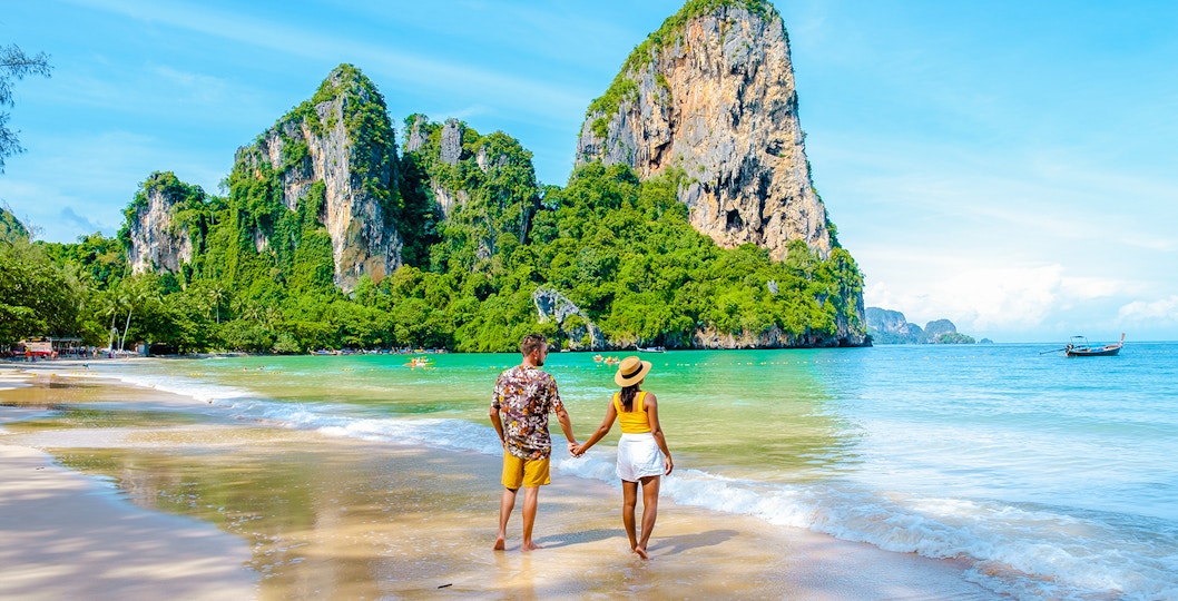 Couple walking on Railay Beach with limestone cliffs in Krabi, Thailand.