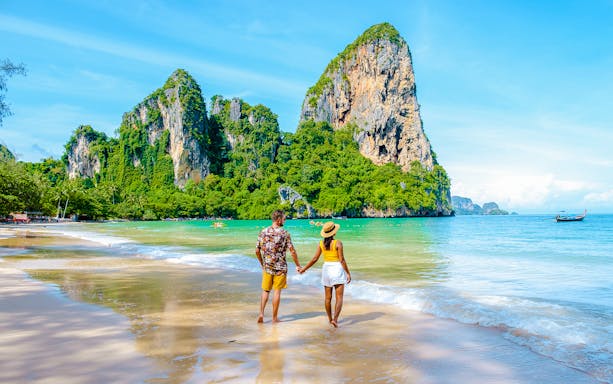 Couple walking on Railay Beach with limestone cliffs in Krabi, Thailand.