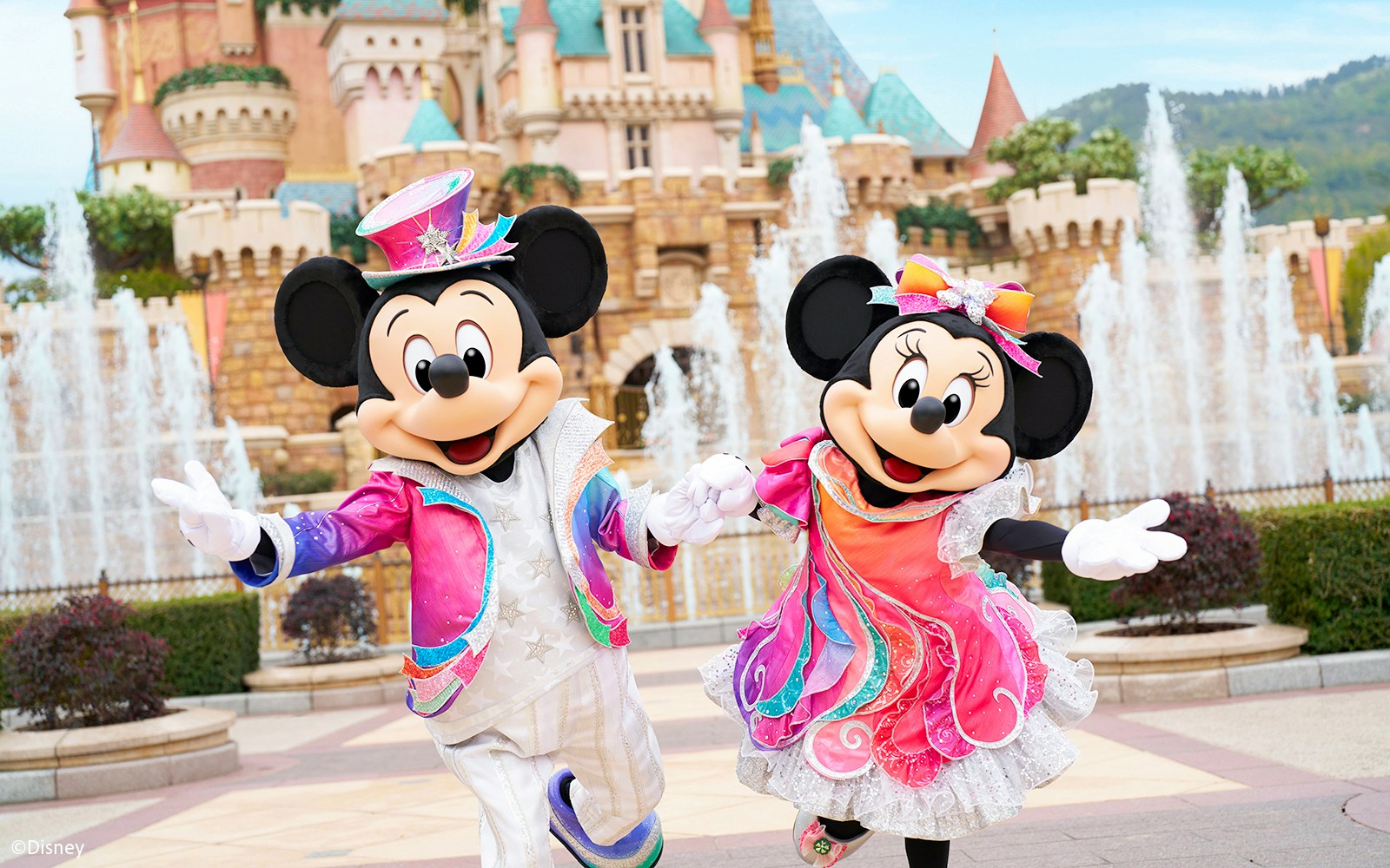 Mickey and Minnie Mouse in colorful outfits at Disneyland Hong Kong with castle backdrop.