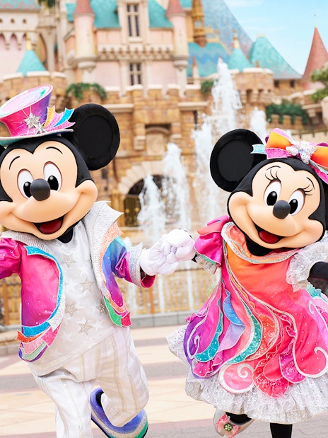 Mickey and Minnie Mouse in colorful outfits at Disneyland Hong Kong with castle backdrop.