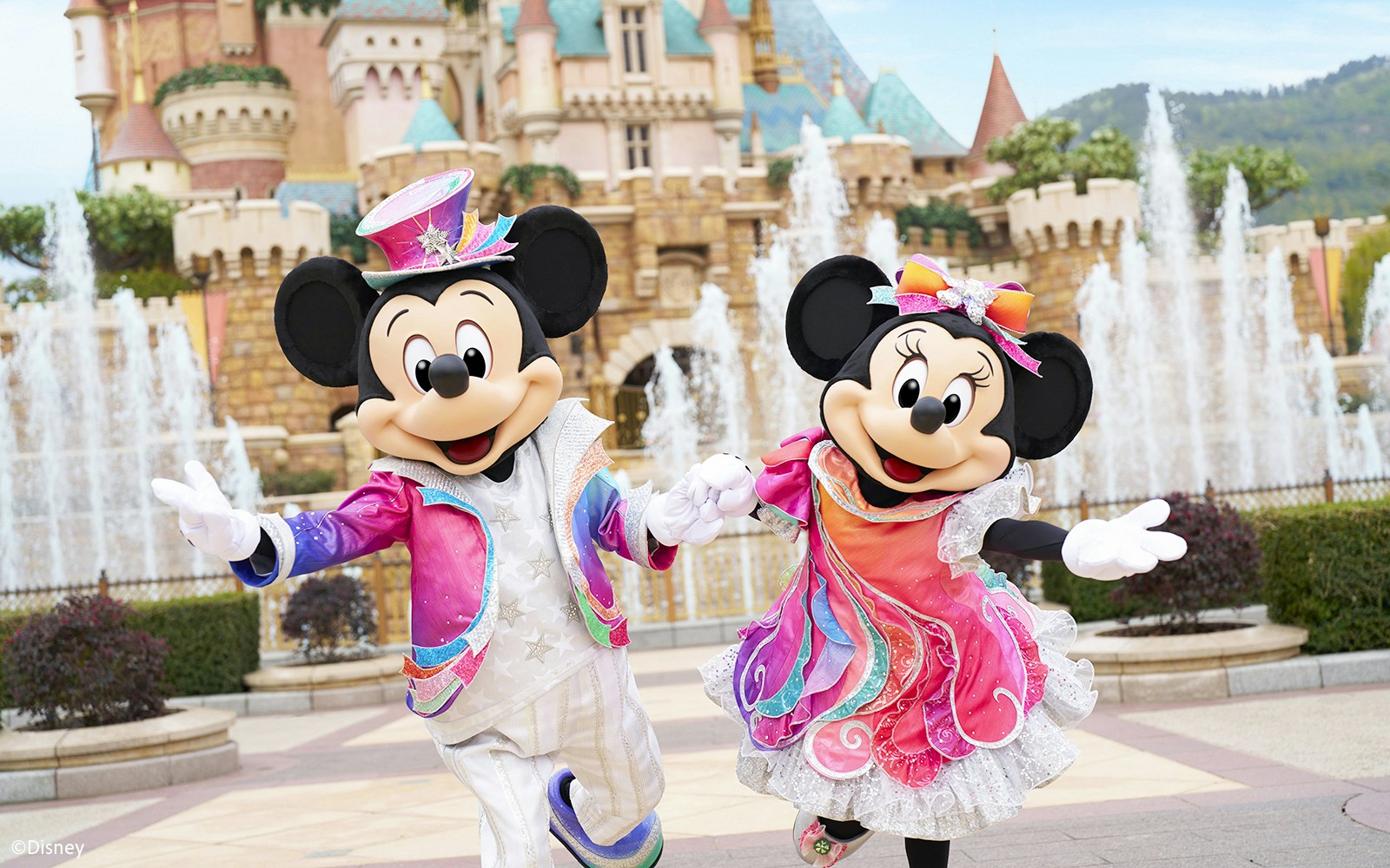Mickey and Minnie Mouse in colorful outfits at Disneyland Hong Kong with castle backdrop.