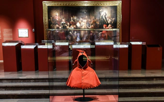 Krakow museum exhibit featuring historical red cloak and large painting in background.