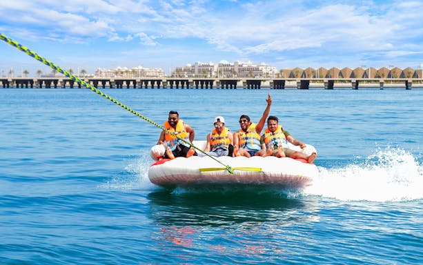 Group enjoying a donut ride on the water with a scenic pier in the background.