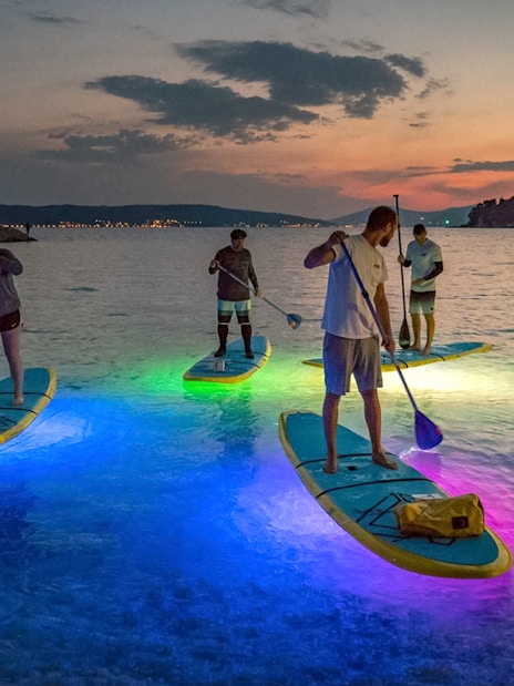 Paddleboarders on illuminated boards during SUP Glow Tour in Split at sunset.