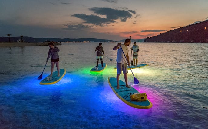 Paddleboarders on illuminated boards during SUP Glow Tour in Split at sunset.