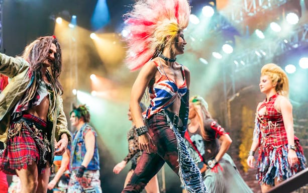 Performers in vibrant costumes on stage during We Will Rock You show.