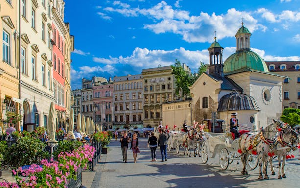 Horse-drawn carriages and pedestrians in Krakow's Old Town Market Square.