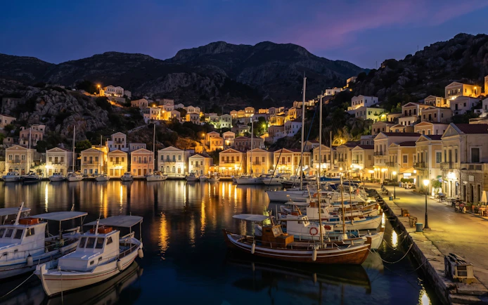 Symi Harbour illuminated at night with boats and hillside houses, Greece.