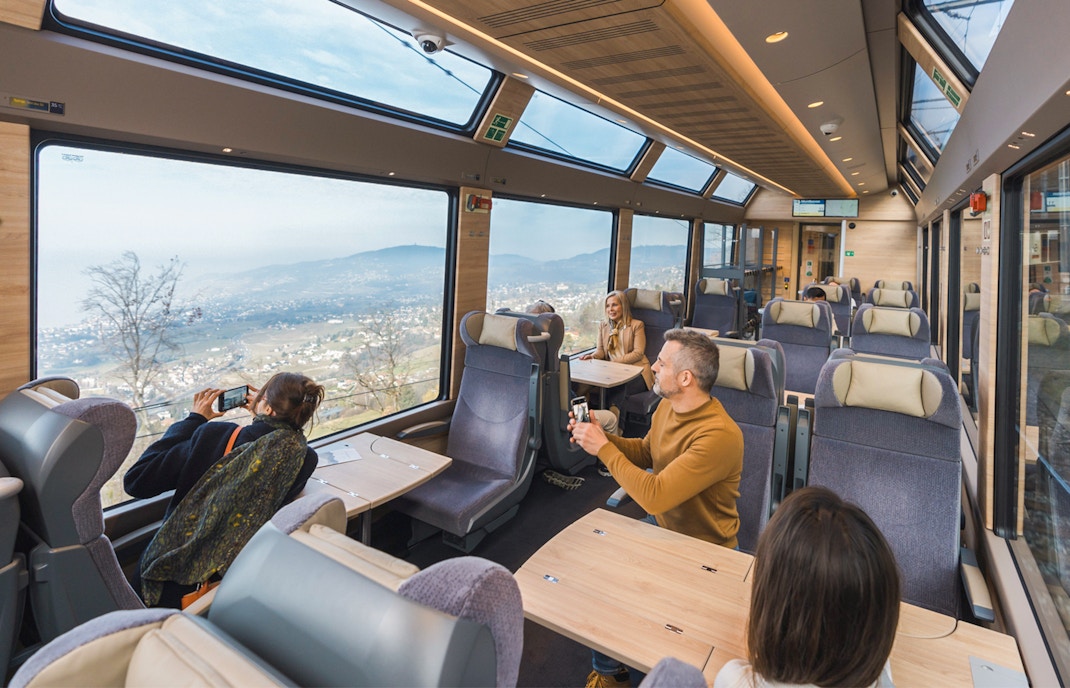 Passengers enjoying the picturesque view from the GoldenPass Express Scenic Train traveling from Montreux to Interlaken, showcasing Switzerland's stunning landscapes.