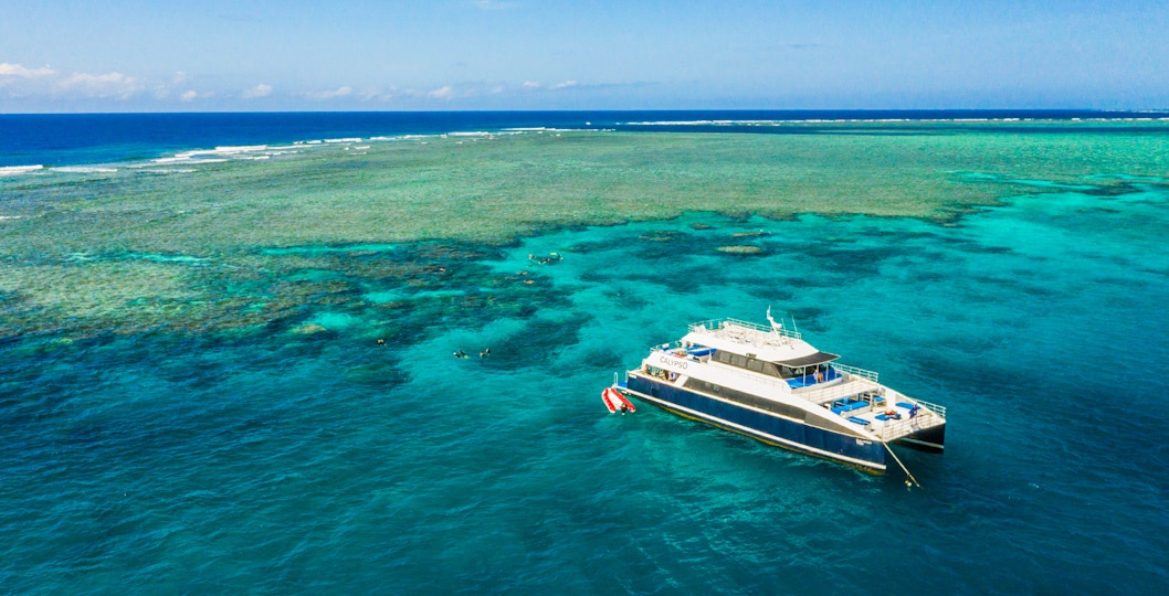 Cruise ship near Great Barrier Reef with snorkelers exploring coral formations.