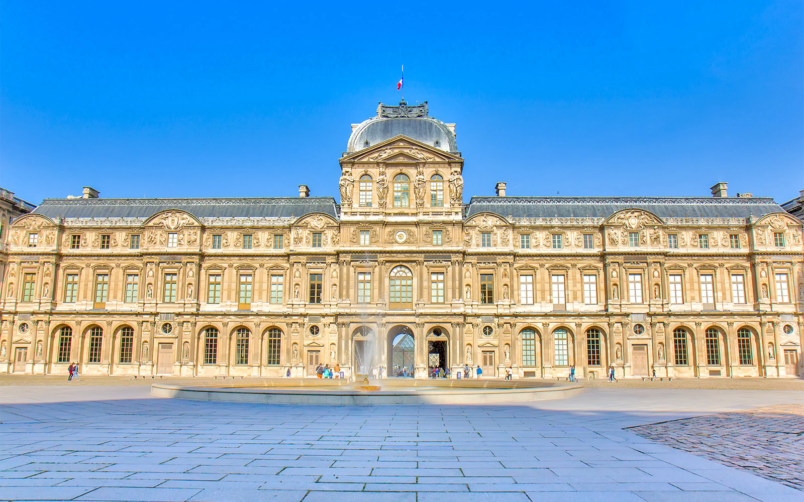 Louvre Museum facade with courtyard and fountain in Paris, France.