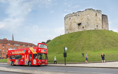 Red double-decker bus on York Hop-On-Hop-Off Tour passing Clifford's Tower in York, England.