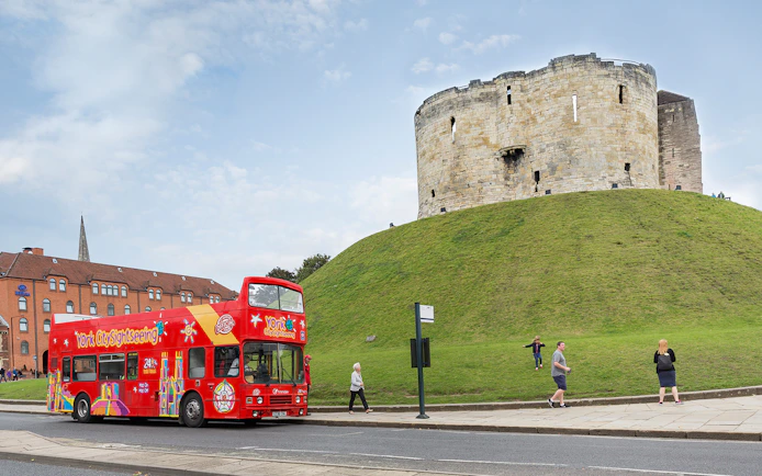 Red double-decker bus on York Hop-On-Hop-Off Tour passing Clifford's Tower in York, England.