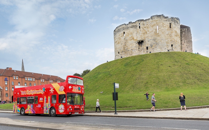 Red double-decker bus on York Hop-On-Hop-Off Tour passing Clifford's Tower in York, England.