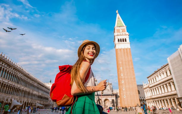 Traveler with a red backpack at San Marco Square, Venice, near St Mark's Bell Tower.
