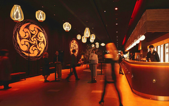 Visitors in the lobby of DRUM TAO Theater Kyoto with decorative lighting and wall art.