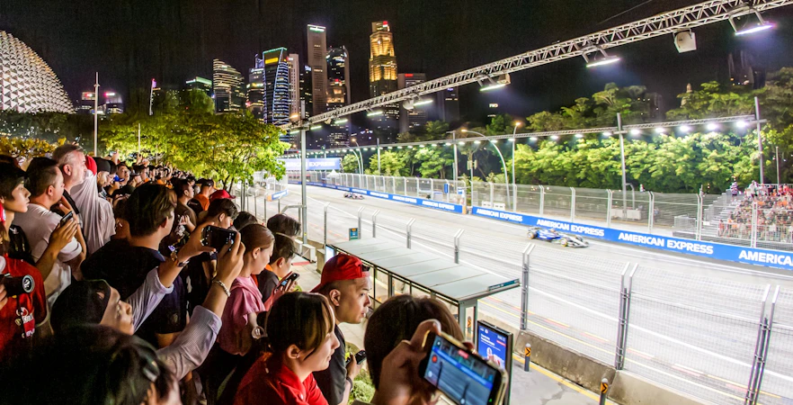 Fans watching a night race from platforms with Singapore skyline in the background.