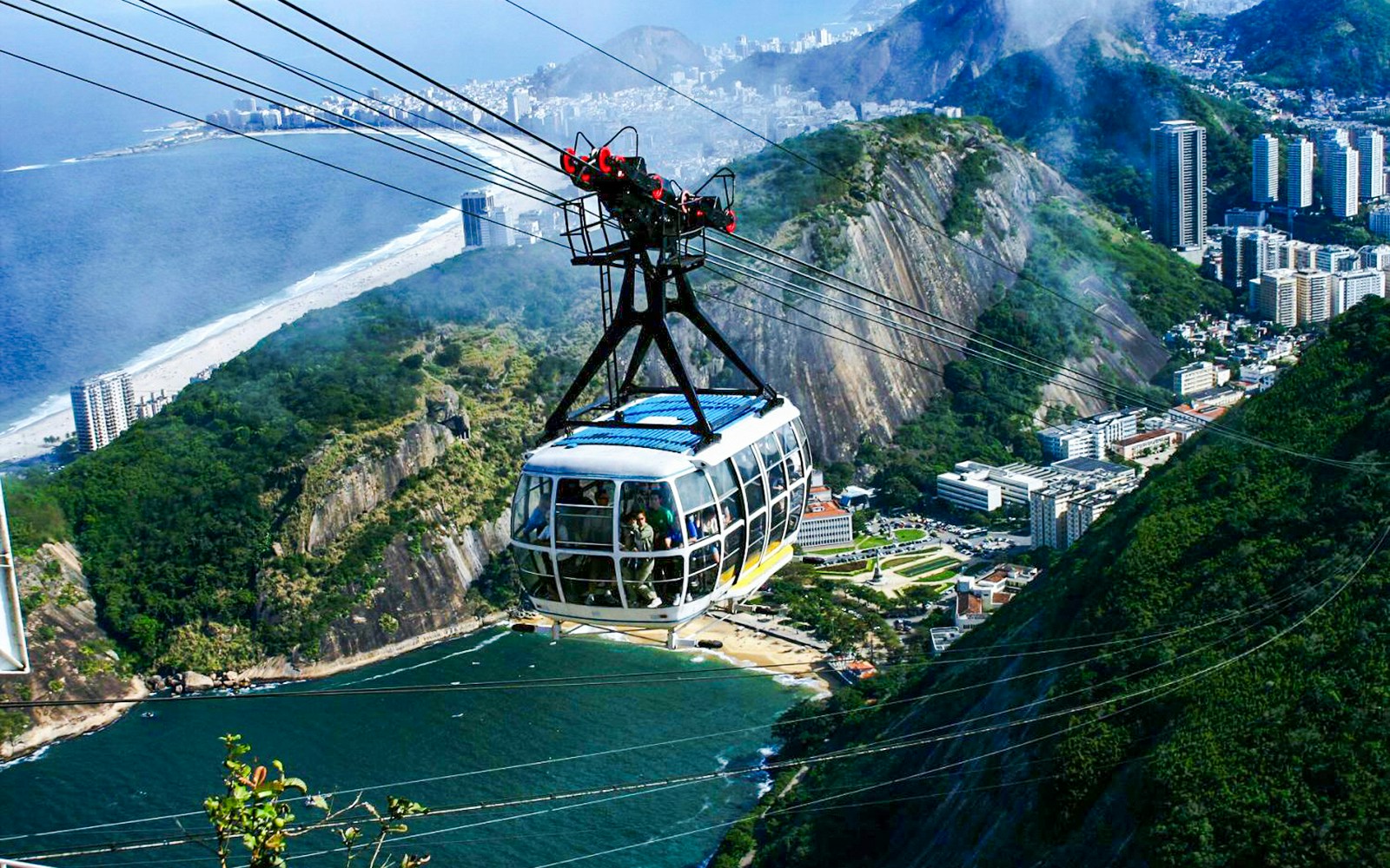 Cable car ascending Sugarloaf Mountain, Rio de Janeiro, with cityscape and ocean view.