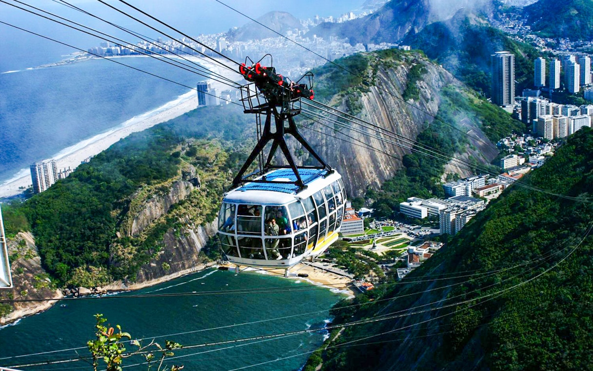 Cable car ascending Sugarloaf Mountain, Rio de Janeiro, with cityscape and ocean view.