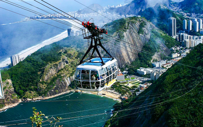 Cable car ascending Sugarloaf Mountain, Rio de Janeiro, with cityscape and ocean view.