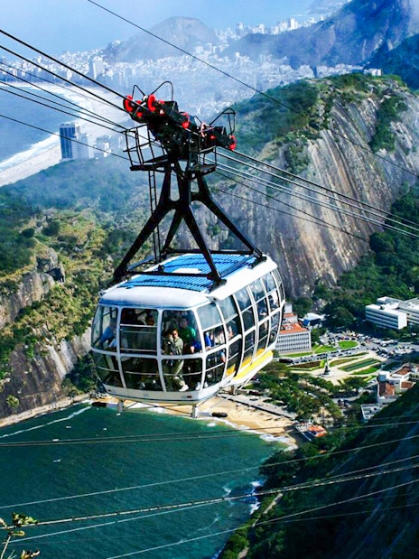 Cable car ascending Sugarloaf Mountain, Rio de Janeiro, with cityscape and ocean view.